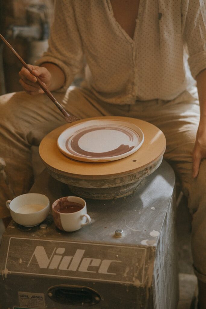 An artisan decorates a ceramic plate on a pottery wheel in an intimate workshop setting.