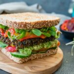 burger with tomato and lettuce on brown wooden round plate