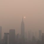 a foggy city skyline with the sun in the distance due to wildfire smoke