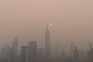 a foggy city skyline with the sun in the distance due to wildfire smoke