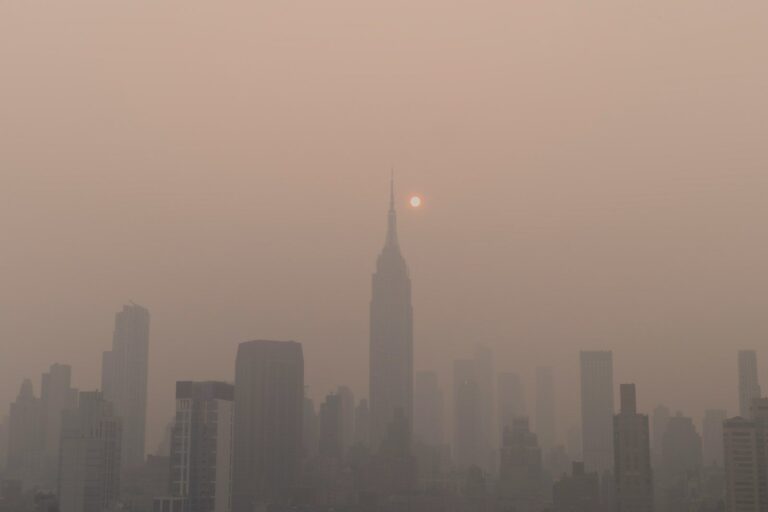 a foggy city skyline with the sun in the distance due to wildfire smoke