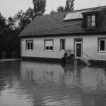 A monochrome image of a suburban house affected by floodwaters.