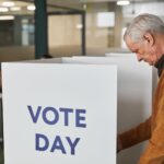 Senior man in brown sweater voting at an indoor polling station on election day.