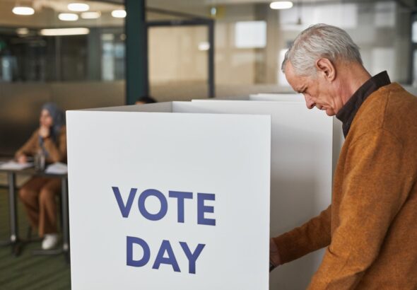 Senior man in brown sweater voting at an indoor polling station on election day.