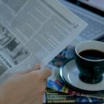 Person reading the morning news at a desk with coffee and a laptop