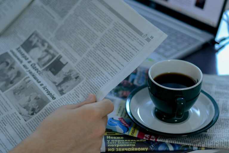 Person reading the morning news at a desk with coffee and a laptop